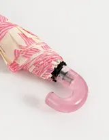 Paraguas corto con estampa de moños y corazones rosas sobre fondo crema, con mango curvo de plástico transparente color rosa.
