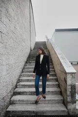 Blazer negra entallada con cuello solapa, manga larga con hombreras, bolsillos delanteros con solapa y cierre frontal con botones dorados.