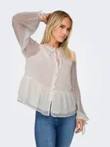 Blusa blanca con textura de lunares, cuello con volantes y lazo, cierre frontal con botones, mangas largas abullonadas con puños elásticos y corte peplum.