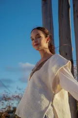 Chaleco tejido color crudo con aplique de cuero marrón en el cuello y detalle de pespunte en el contorno.