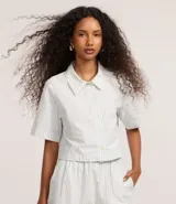 Camisa corta de sarga a rayas verticales celestes y blancas, con cuello inglés, mangas cortas y abotonadura frontal.