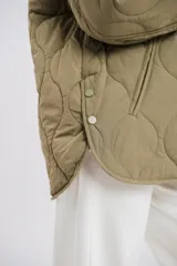 Campera verde militar capitoneada con cuello redondo, cierre frontal con botones a presión, bolsillos laterales y corte recto.
