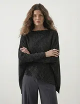 Poncho de tejido lurex color verde oliva con brillo sutil, de corte amplio y manga larga con puños acanalados. Presenta un bajo asimétrico con caída diagonal.