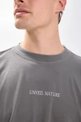 Camiseta manga corta gris oscuro con estampa de un paisaje marino y texto en color blanco. Corte amplio y recto, con proporciones cuadradas.