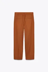 Pantalón color marrón confeccionado en hilatura con mezcla de lyocell y algodón. Tiro medio, cintura con trabillas, bolsillos laterales, pinzas en delantero y raya planchada. Cierre frontal con cremallera, botón y ganchos metálicos.