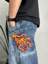Pantalón de jean celeste con corte holgado y parches bordados de llamas en los bolsillos traseros.
