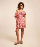 Vestido corto de viscosa y lino con estampado de olas en color blanco sobre fondo rojo. Tiene escote off-shoulder, mangas cortas holgadas, lazo en el busto con detalle de abalorios y volado en el bajo.