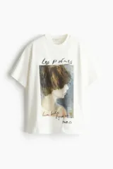 Remera color crudo de corte recto y mangas cortas, con estampado de una pintura de una mujer y texto en francés.