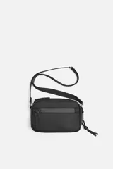 Bandolera negra de acabado engomado con correa ajustable y extraíble. Tiene un compartimento principal con cierre de cremallera, un bolsillo interior con cremallera y un bolsillo frontal con cremallera.