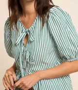 Blusa de tricolina a rayas verticales blancas y verdes, con cuello redondo, mangas cortas abullonadas y lazos delanteros.