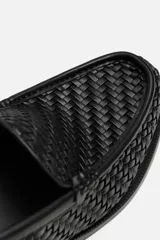 Mocasín de cuero negro con diseño trenzado en la parte superior, horma redonda y suela con ligero tacón.
