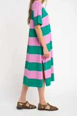 Vestido midi de tejido suave y ligero, con cuello redondo y mangas cortas. Presenta un patrón de rayas horizontales anchas en color verde oscuro y rosado. El vestido tiene aberturas laterales en el ruedo.