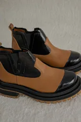 Botas Chelsea de cuero color camel con paneles laterales elásticos negros y puntera de charol negro. Tienen una suela track gruesa en negro y camel.