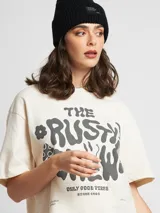 Remera cruda de algodón con estampa frontal con el texto "The Rusty Crew" y un dibujo de una cara sonriente.