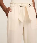 Pantalón carrot de sarga color crudo, con cintura elástica, lazo ajustable y bolsillos laterales.