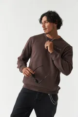 Buzo de felpa color gris claro, con cuello redondo, mangas largas y costuras a contratono. Presenta lettering estampado en el pecho, bolsillos laterales y logo en grifa de goma.