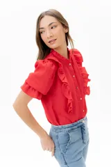 Blusa de lino color rojo con volados frontales que enmarcan el pecho, cuello redondo con mini volado y mangas 3/4 abullonadas con puño elástico. Presenta un cierre frontal con botones y una silueta relajada.