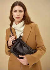Bandolera negra de cuero sintético con solapa y cierre magnético. Tiene correa de hombro ajustable con detalle de nudo.