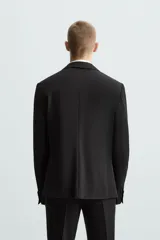 Blazer slim fit negra confeccionada en tejido con viscosa. Tiene cuello con solapas de muesca, manga larga con puño con detalle de botones, bolsillo de vivo en pecho, bolsillos de solapa en cadera, bolsillo interior, bajo con aberturas en espalda y cierre frontal con botones.