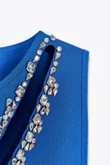 Vestido midi azul de punto, sin mangas y cuello redondo. Presenta un corte diagonal en el frente con detalle de apliques de strass.