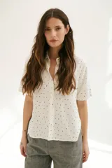 Camisa blanca con estampado de lunares negros, de corte clásico, manga corta y cuello camisero.