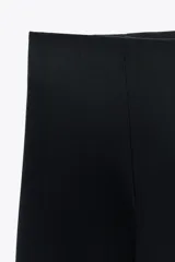 Pantalón negro de tiro alto y corte acampanado, con cierre frontal de cremallera dorada.