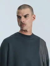 Buzo negro de corte holgado con paneles superpuestos en diferentes texturas y bolsillo de parche con botón a presión en el frente.