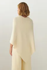 Ruana color crema de tejido de punto industrial con terminación en contraste de color. Tiene doble ojal para mantener el cruce.