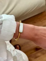 Pulsera dorada rígida con dije rectangular de piedra blanca.