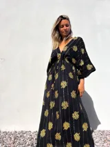 Vestido túnica largo negro con estampado dorado de flores y rayas verticales.