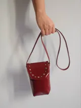 Cartera porta celular de cuero color rojo con correa larga y tachas doradas.