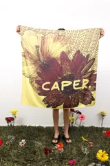 Pañuelo cuadrado de 1 metro x 1 metro, color amarillo con estampado de flores grandes en tonos bordó y rojo. Incluye el texto "CAPER" en amarillo y un patrón repetitivo de la palabra "CAPER" en el fondo.