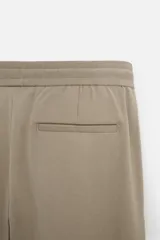 Pantalón color arena de corte recto, confeccionado en tejido elástico. Cuenta con cintura elástica ajustable con cordón, bolsillos laterales y bolsillos de vivo en la parte trasera.