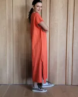 Vestido largo color crudo con cuello redondo y mangas cortas con ribete negro. Tiene corte recto y aberturas laterales en el ruedo.