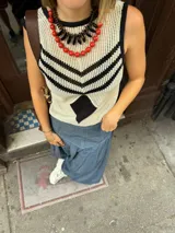 Chaleco calado negro con diseño de rayas diagonales rojas, beige y blancas.