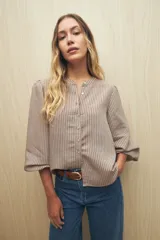 Camisa color crema a rayas verticales finas, de cuello mao, mangas 3/4 abullonadas con elástico en los puños y cierre frontal con botones de nácar.