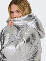 Campera puffer plateada con capucha, cierre frontal con cremallera y botones a presión, bolsillos delanteros con solapa y cordón ajustable en el dobladillo.
