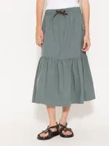 Pollera midi color verde grisáceo, confeccionada en poplín liviano. Presenta cintura elastizada con cordón ajustable, bolsillos tipo plaque con fuelle y tapa, y un recorte con volado fruncido en el ruedo.