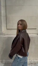Campera marrón de ecocuero con cuello clásico, corte holgado y cierre frontal con botones a presión.