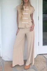 Blusa sin mangas color beige claro, confeccionada en lino tusor. Presenta cuello mao y cierre frontal con tres nudos chinos blancos. Los bordes de la abertura frontal tienen un acabado deshilachado.