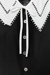 Blazer negro de cuello redondo y manga larga con hombreras. Incluye cuello desmontable blanco con detalle de puntilla. Cierre frontal con botones.