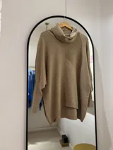 Polerón color camel de corte oversize, con cuello drapeado y mangas largas caídas. La parte delantera es más corta que la trasera.