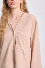Blusa color beige de manga larga, con cuello en V y cierre frontal con botones.