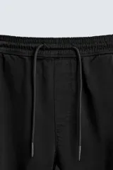Pantalón jogger negro de corte slim fit, confeccionado en tejido de algodón con cintura elástica ajustable con cordón, bolsillos frontales y traseros de vivo, y bajo con puño elástico.
