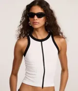 Musculosa blanca sin mangas, con cuello redondo y cierre frontal con cremallera. Presenta detalles contrastantes en negro en cuello y sisas. Diseño seamless.