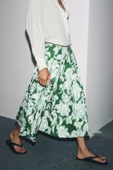 Falda midi de tiro medio con estampado floral en tonos blanco y celeste sobre fondo verde. Presenta detalle de tablas y cierre lateral con cremallera oculta.