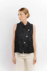 Chaleco de jean sin mangas con cuello en V y cierre frontal con botones metálicos. Tiene dos bolsillos de parche en el pecho y corte recto.