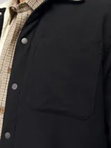 Sobrecamisa negra de manga larga con cuello clásico y fit relajado. Tiene cierre de botones, un bolsillo en el pecho y forro interno de borreguito color crema.