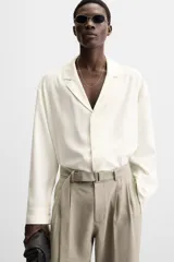 Pantalón negro de corte amplio, con pliegues frontales, bolsillos laterales y traseros de ojal. Incluye cinturón de la misma tela con hebilla metálica.