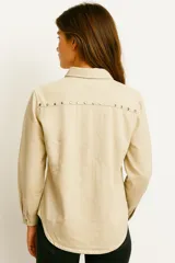 Camisa de jean negra con cuello clásico, cierre frontal con botones a presión, dos bolsillos con solapa en el pecho y tachas plateadas decorativas en cuello, hombros y bolsillos.